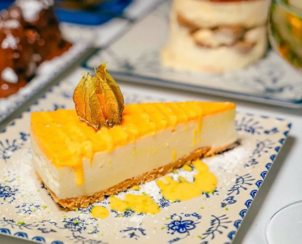 A slice of cheesecake with a golden glaze and physalis on a blue-and-white plate
