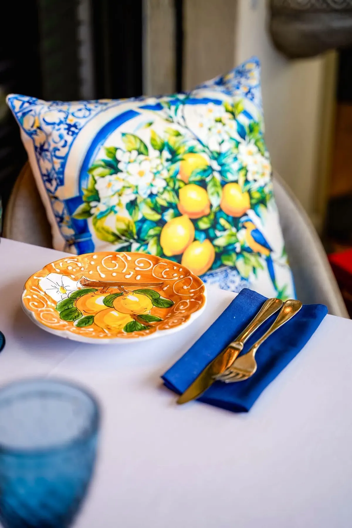 A blue-and-white lemon-print cushion beside a painted lemon plate and a blue napkin