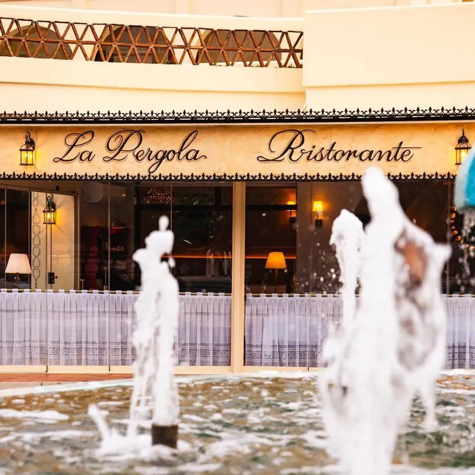 La Pergola Ristorante's illuminated sign behind the fountain on the square