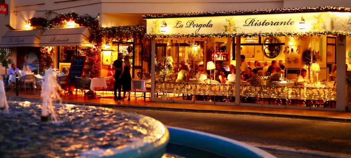 The restaurant lit up at night, across the fountain