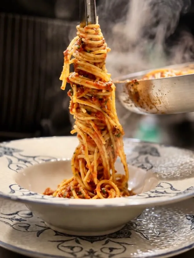 Spaghetti in tomato sauce lifted from a pan into a blue-patterned bowl